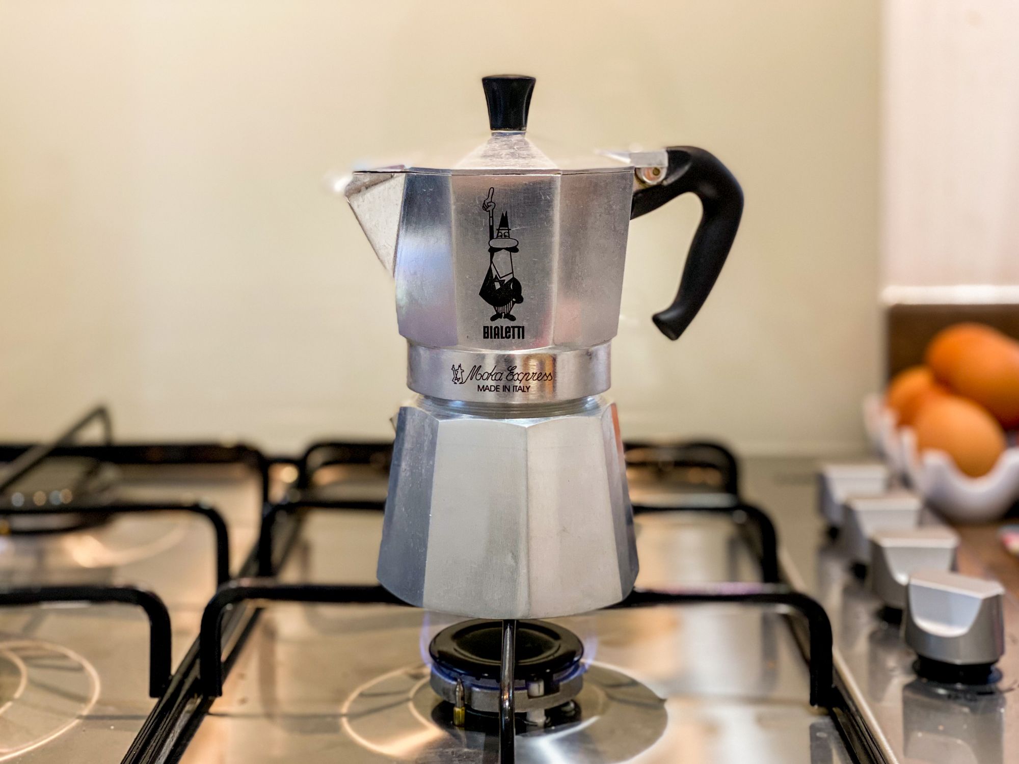 A silver Moka Pot brewing on a kitchen hob