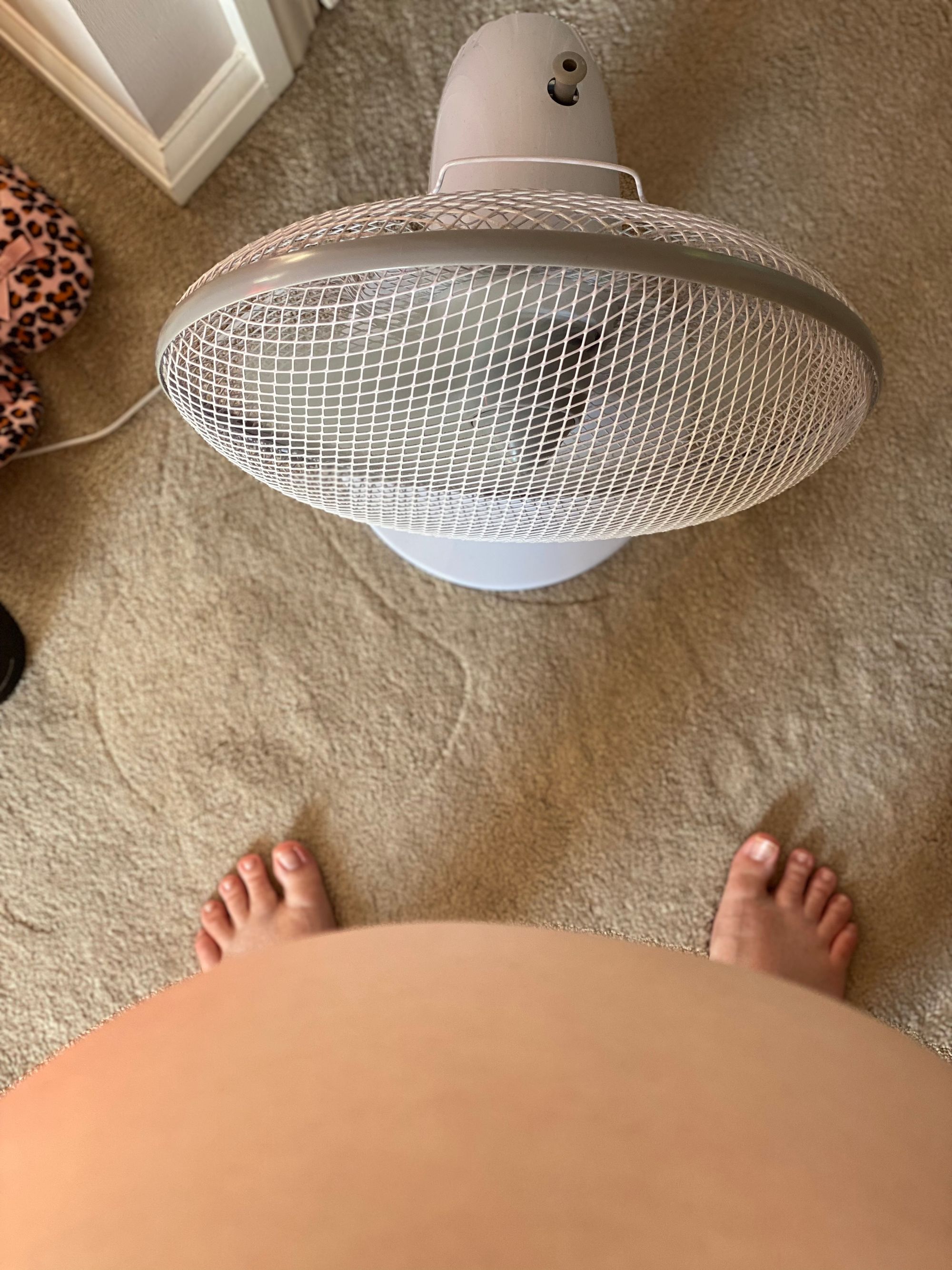 Me standing with my baby bump out, barely able to see my feet, in front of a fan in the hot summer