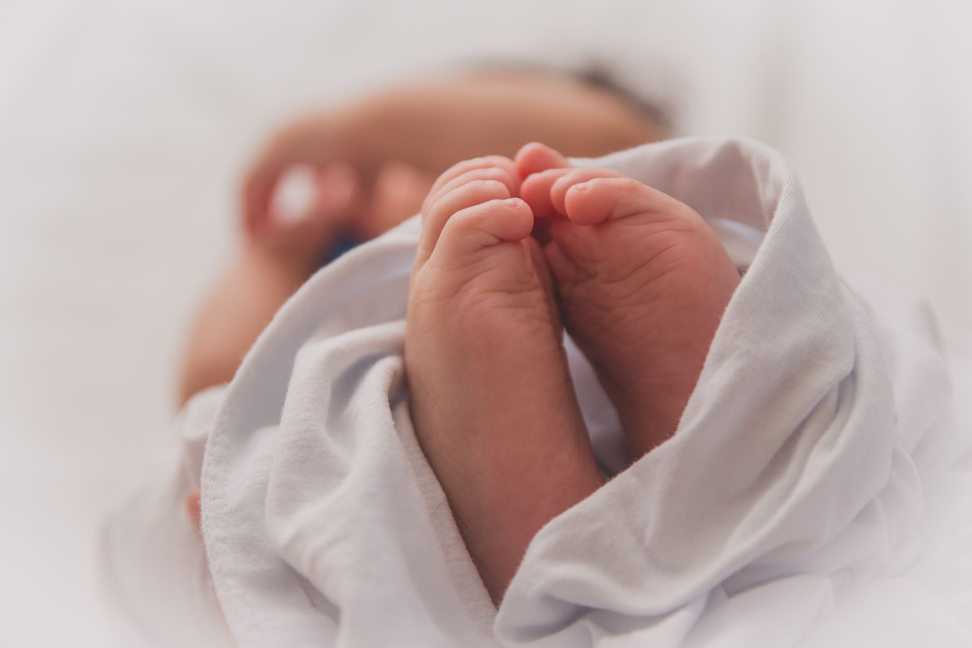 A close up of a very new baby’s feet, with them wrapped in a sheet in the background