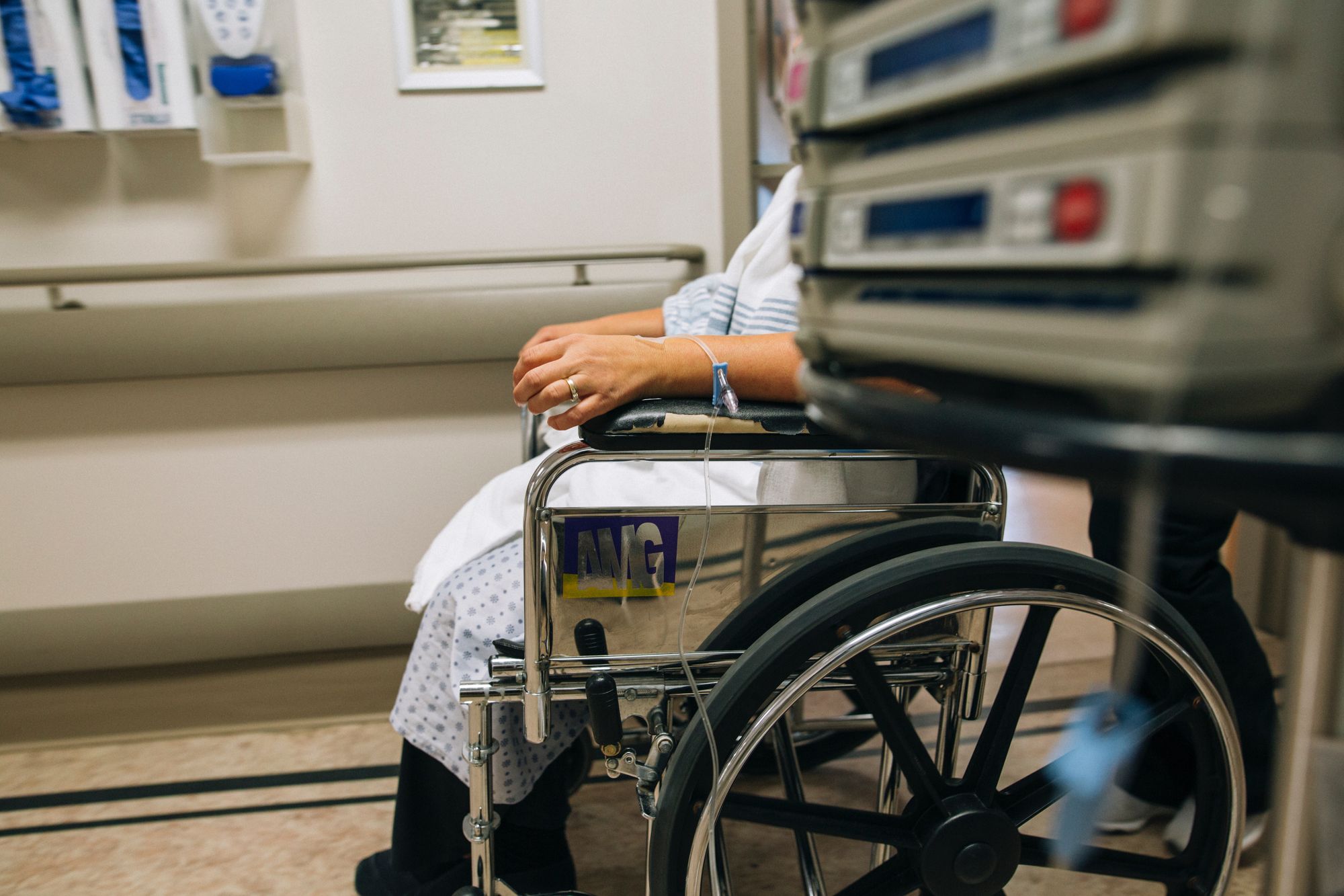 Someone in a hospital gown in a wheelchair - their face is obscured by equipment